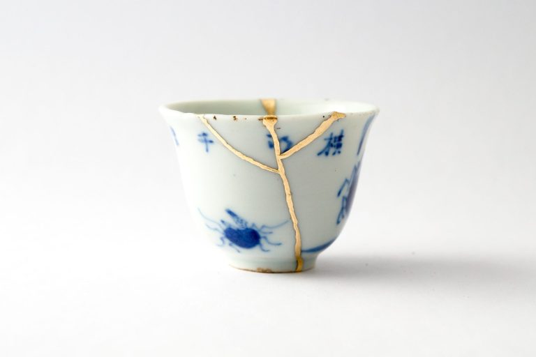 eine weiss-blaue teetasse, die mit vergoldeten klebelinien repariert wurde.
