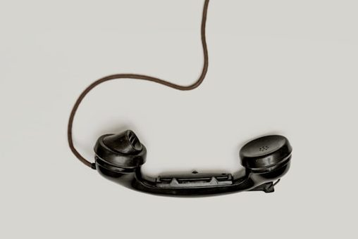 ein alter schwarzer telefonhörer mit schwarzem kabel ist auf grauem hintergrund zu sehen.